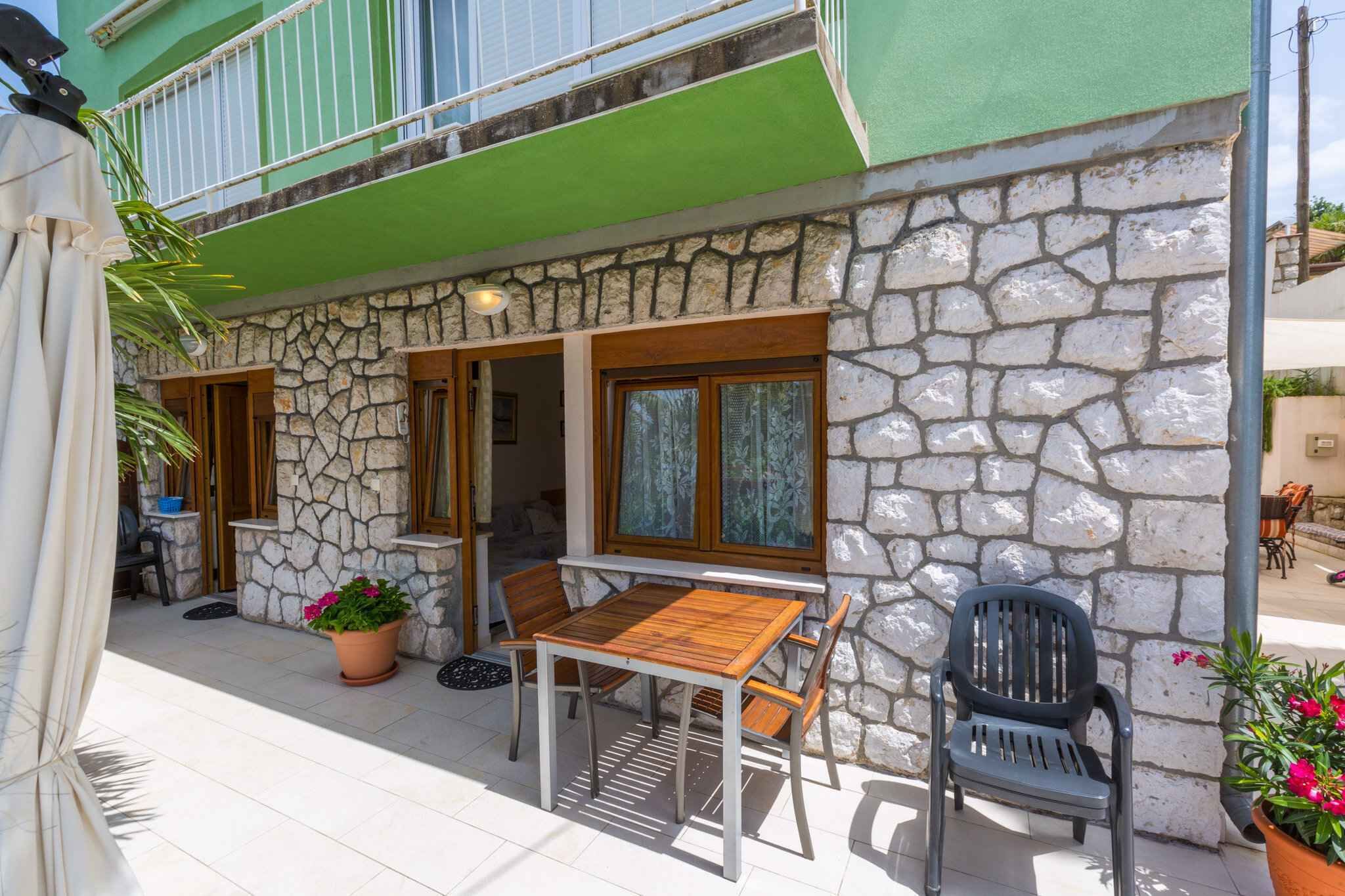 A stone building with a wooden table and chairs outside, a balcony, and a door leading to a room.