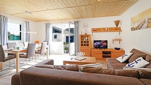 Un soggiorno moderno con soffitto in legno, una TV, un divano, un tavolino da caffè e un'area pranzo con tavolo e sedie.