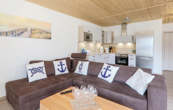 Ein gemütlicher Wohnbereich mit einem braunen Sofa, einem Holztisch und einer Küche im Hintergrund.
