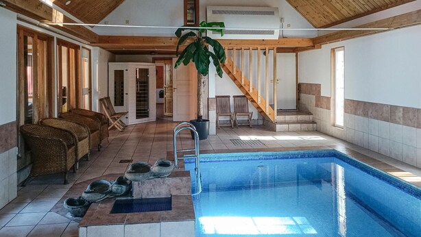 Ein Hallenbad mit Holzbalkendecke, gefliesten Wänden und einer Treppe, die in eine obere Ebene führt.