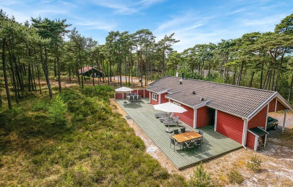 Une cabane rouge dotée d’une terrasse, entourée d’une forêt.