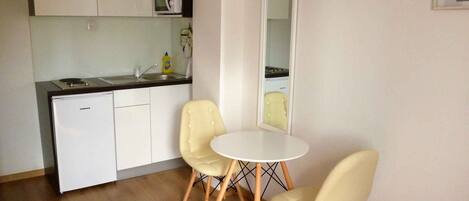 A compact kitchen with white cabinets, a sink, and a microwave. There are two yellow chairs around a small white table.