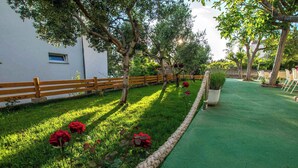 Un jardín con valla de madera, césped artificial verde y rosales rojos.