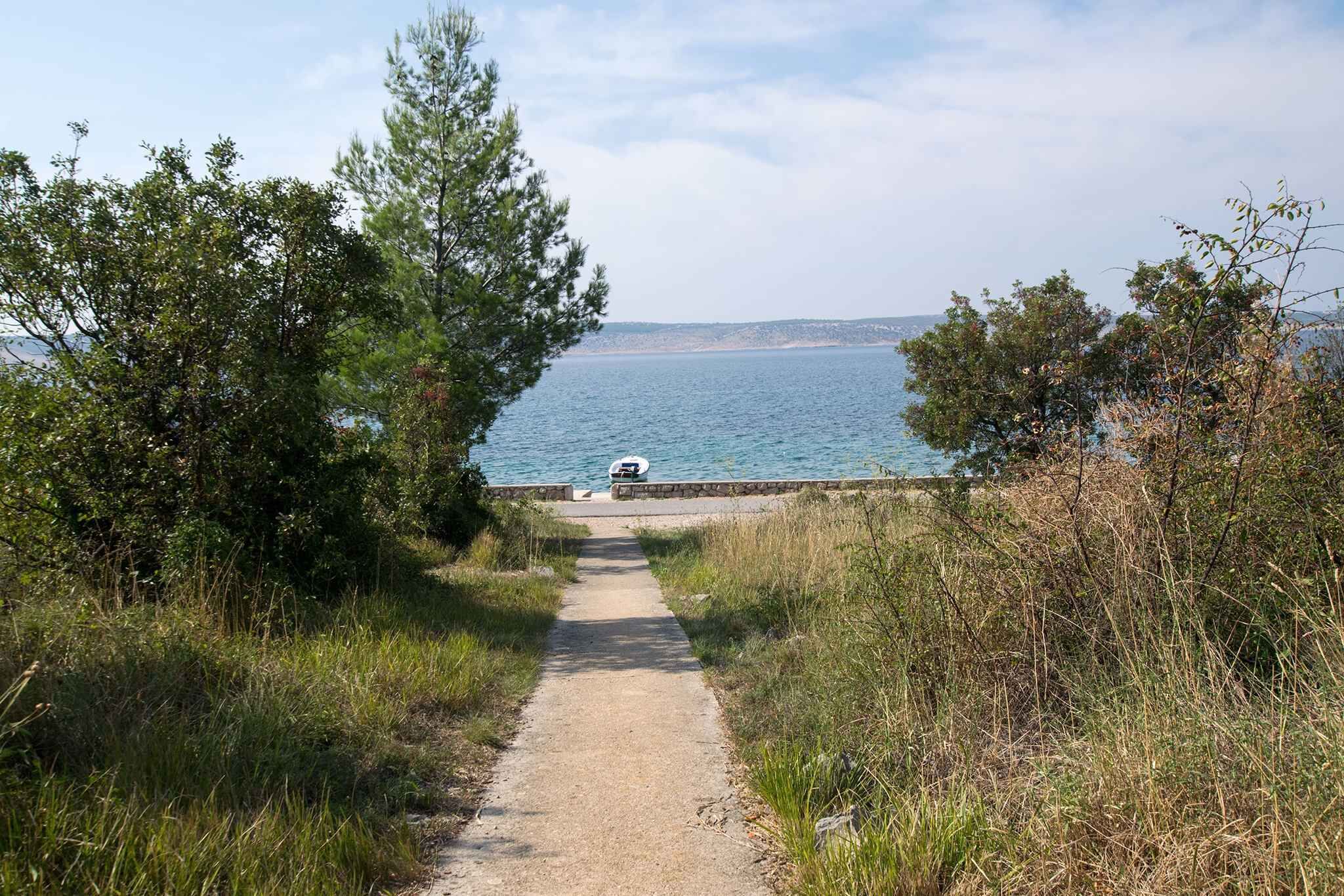 Un sentier côtier menant à une plage où se trouve un bateau, avec une côte rocheuse.