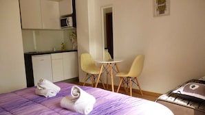 Una habitación de hotel con una cama, una kitchenette pequeña, dos sillas y una mesa.