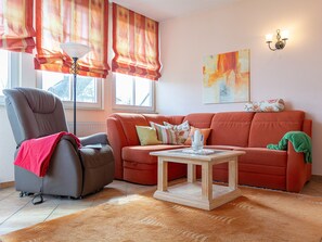 Un salon avec un fauteuil inclinable gris, un canapé orange, une table basse en bois et un lampadaire.