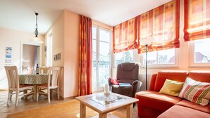 A living room with a sofa, a dining table with chairs, a chair, a lamp, and a window with curtains. - Strandstr. 31 apt. MA-03. - Strandstrasse 31 apt. 03 (Kühlungsborn)