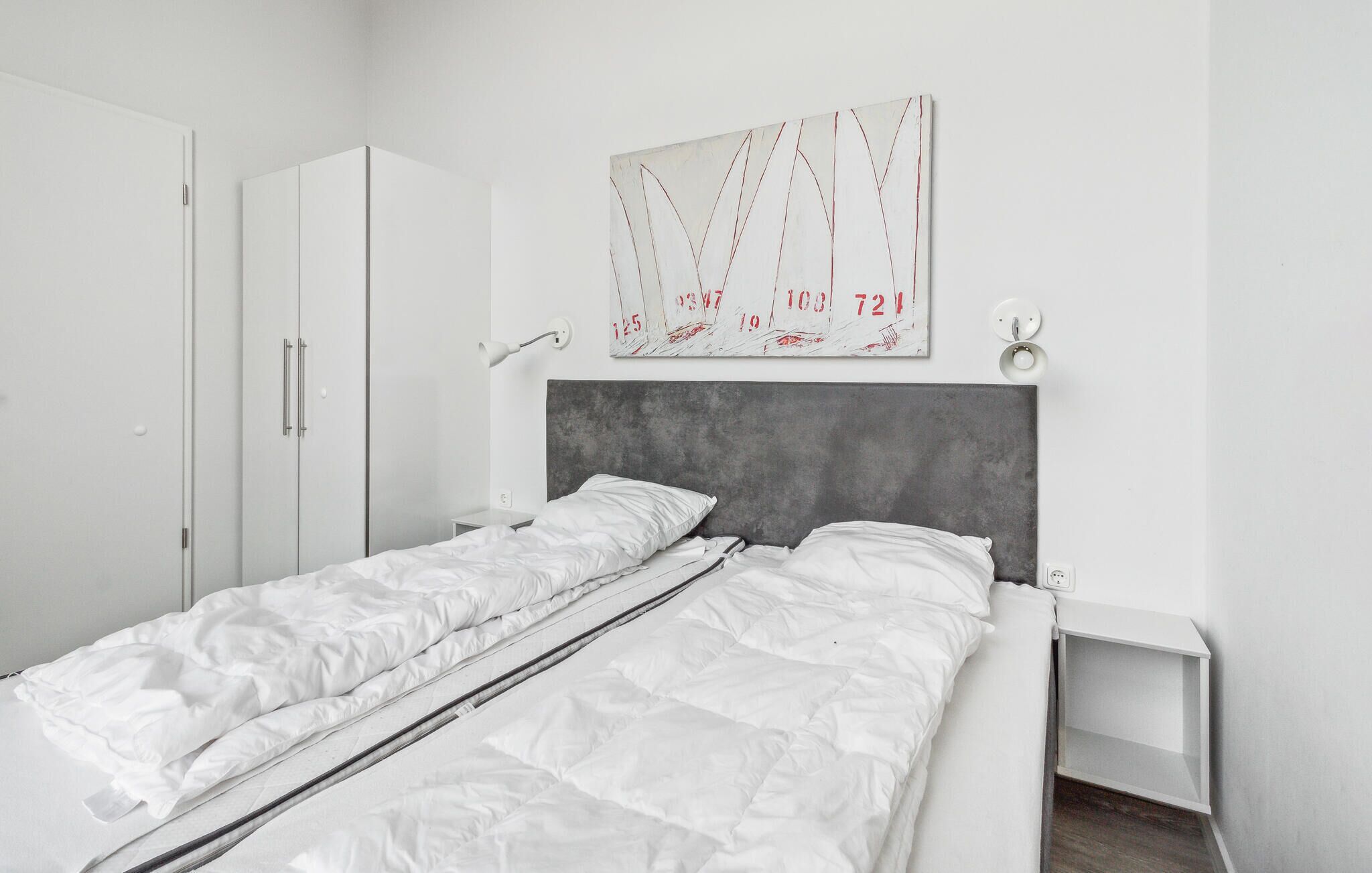 A modern bedroom with a single bed, a wardrobe, a bedside table, and a wall-mounted artwork.