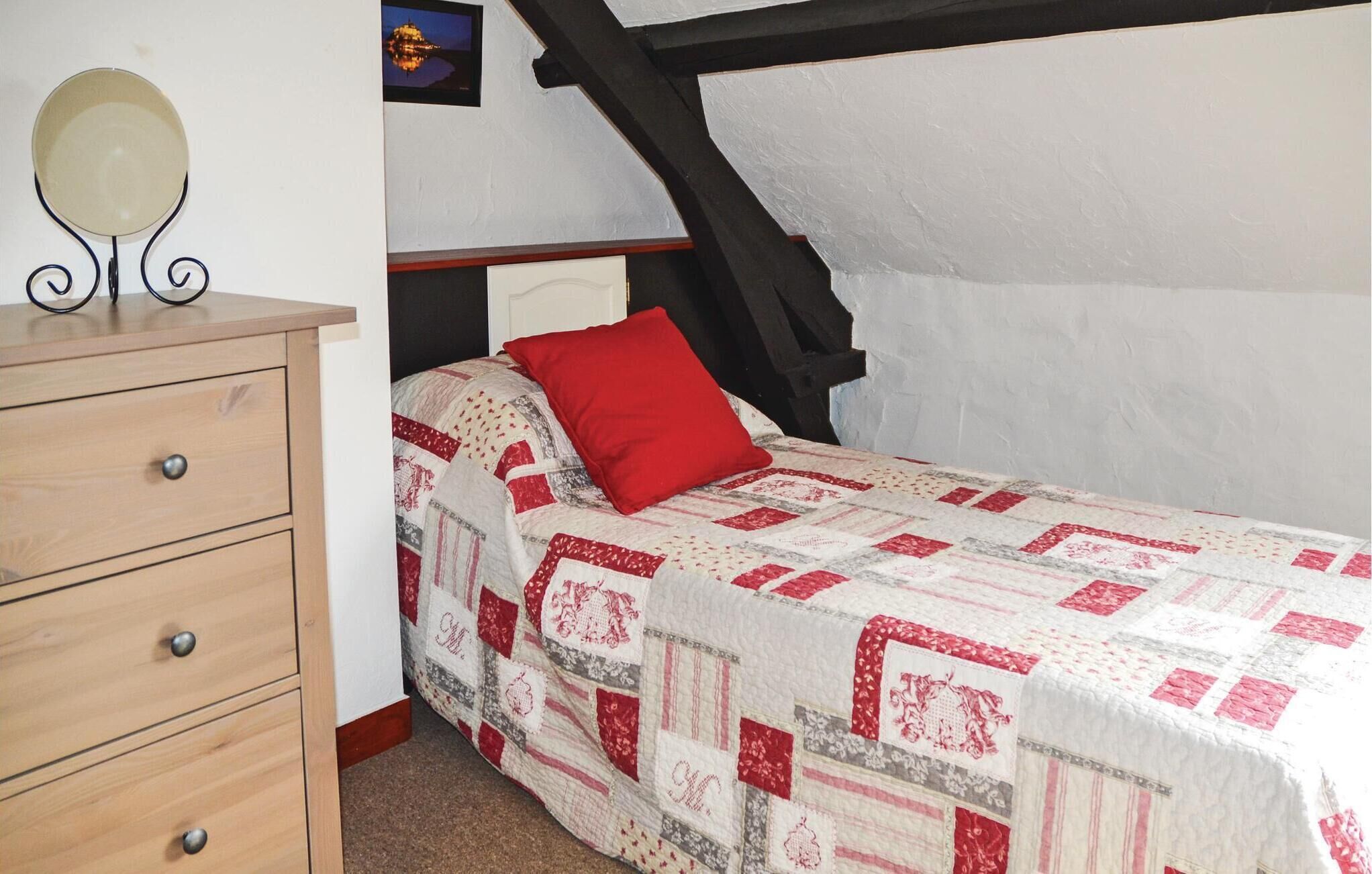 A bedroom with a wooden dresser, a quilted bedspread, a red pillow, and a wall-mounted mirror.