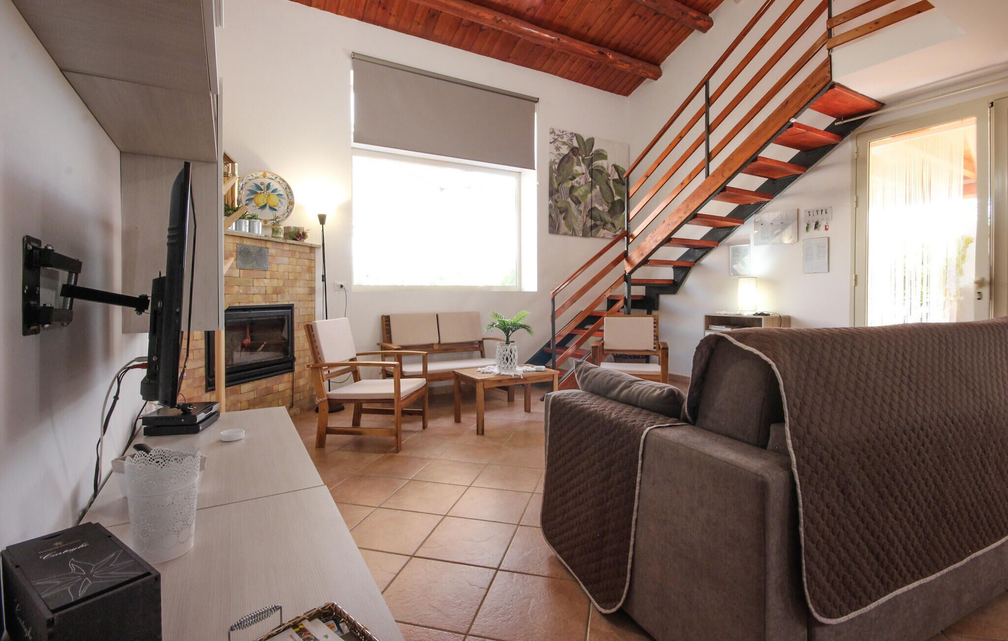 A living room with a fireplace, wooden furniture, a staircase, and a large window.