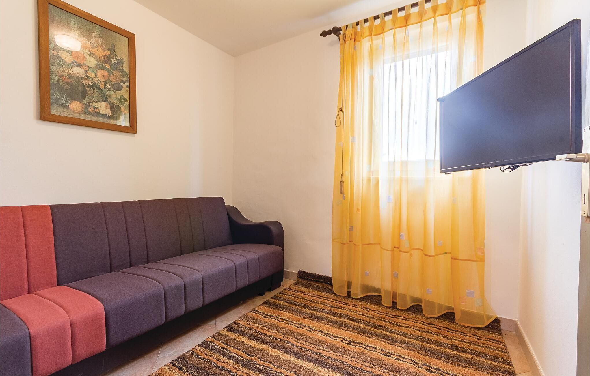 A living room with a sofa, a painting on the wall, a television, and a window with yellow curtains.