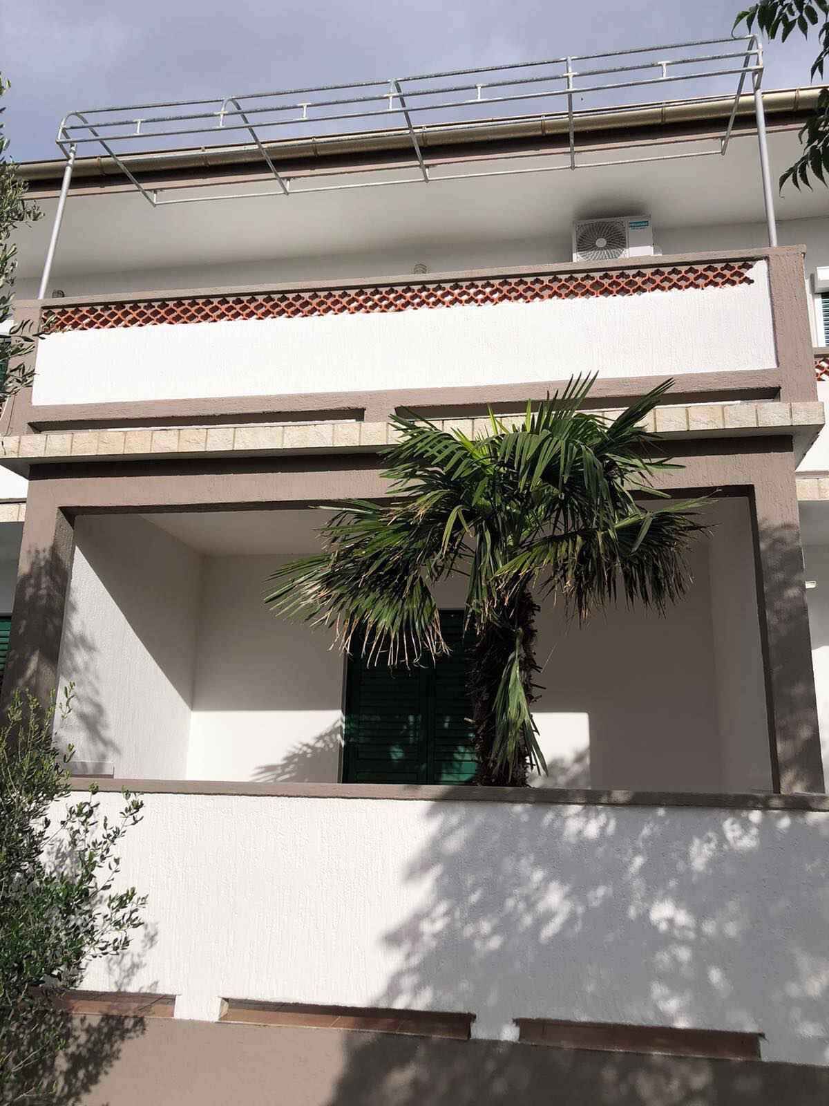 Un edificio a due piani con un balcone, una palma e un tetto in tegole.