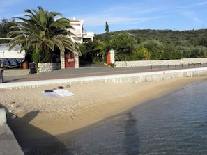 Una platja amb un mur de pedra, una palmera i un edifici al fons.