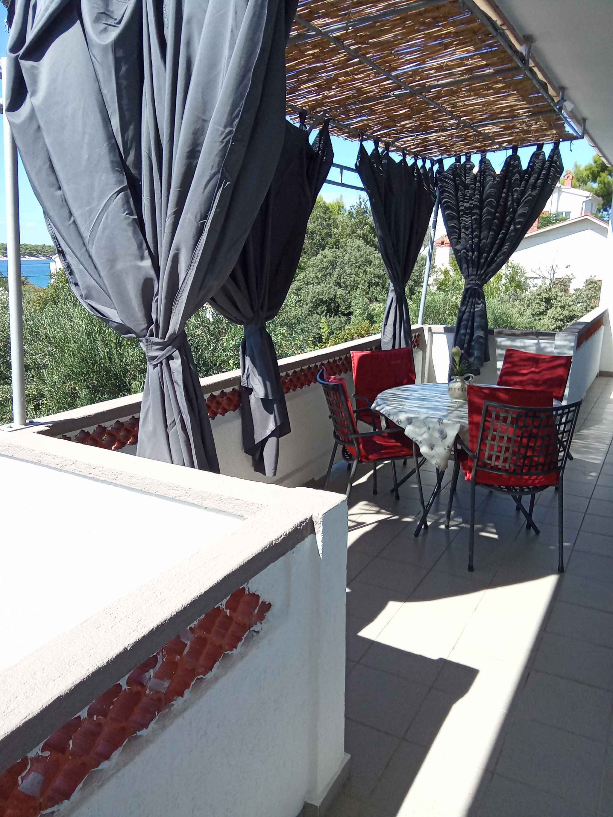 An outdoor terrace with a table and chairs, covered by a striped awning, and surrounded by greenery.