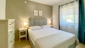 Une chambre à coucher bien rangée, avec un lit, deux tables de chevet dotées de lampes, une commode et deux tableaux encadrés accrochés au mur.