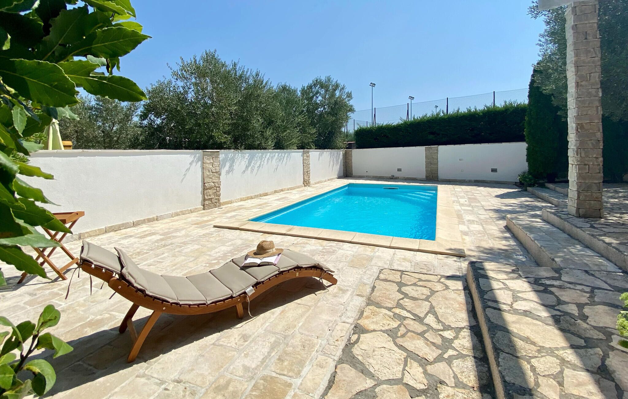 A swimming pool with a stone deck, a lounge chair, and a stone pillar.
