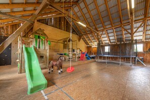 Una amplia arena interior con piso de madera, un caballo y diverso equipo ecuestre.