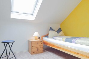 Habitación tipo dormitorio con una cama alta, una mesita de noche, una lámpara y un taburete pequeño.