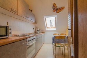 Cocina compacta con microondas, estufa y cafetera. Se aprecia una ventana con cortinas y una decoración de mariposa en la pared.