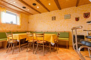 A restaurant interior with wooden ceiling beams, green cushioned benches, and tables with yellow tablecloths.