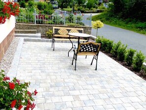 An outdoor patio area with a stone floor, a wooden bench, and a metal table.