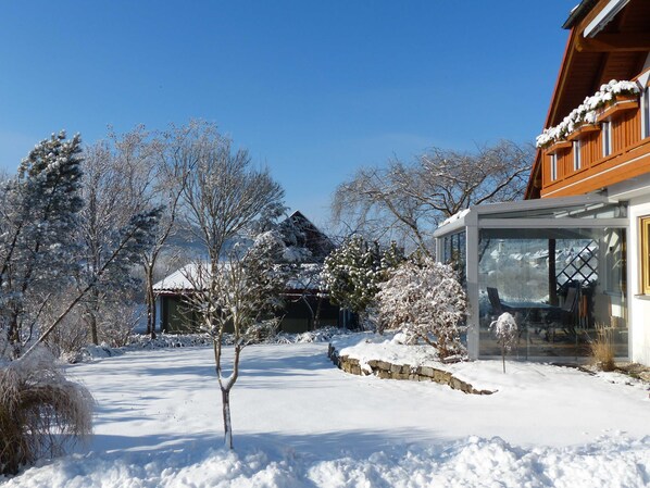A snow-covered landscape with a wooden house and a glass conservatory.