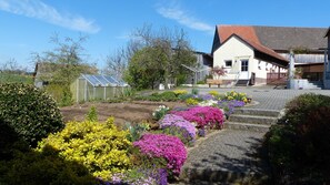 A garden with colorful flowers, a greenhouse, and a building with a red roof.