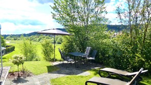 A patio with a table and chairs, a lounge chair, and a view of a green landscape.