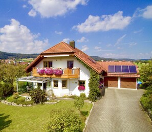 A two-story house with a sloped roof, a balcony with flower boxes, a covered porch, and a garage with solar panels.