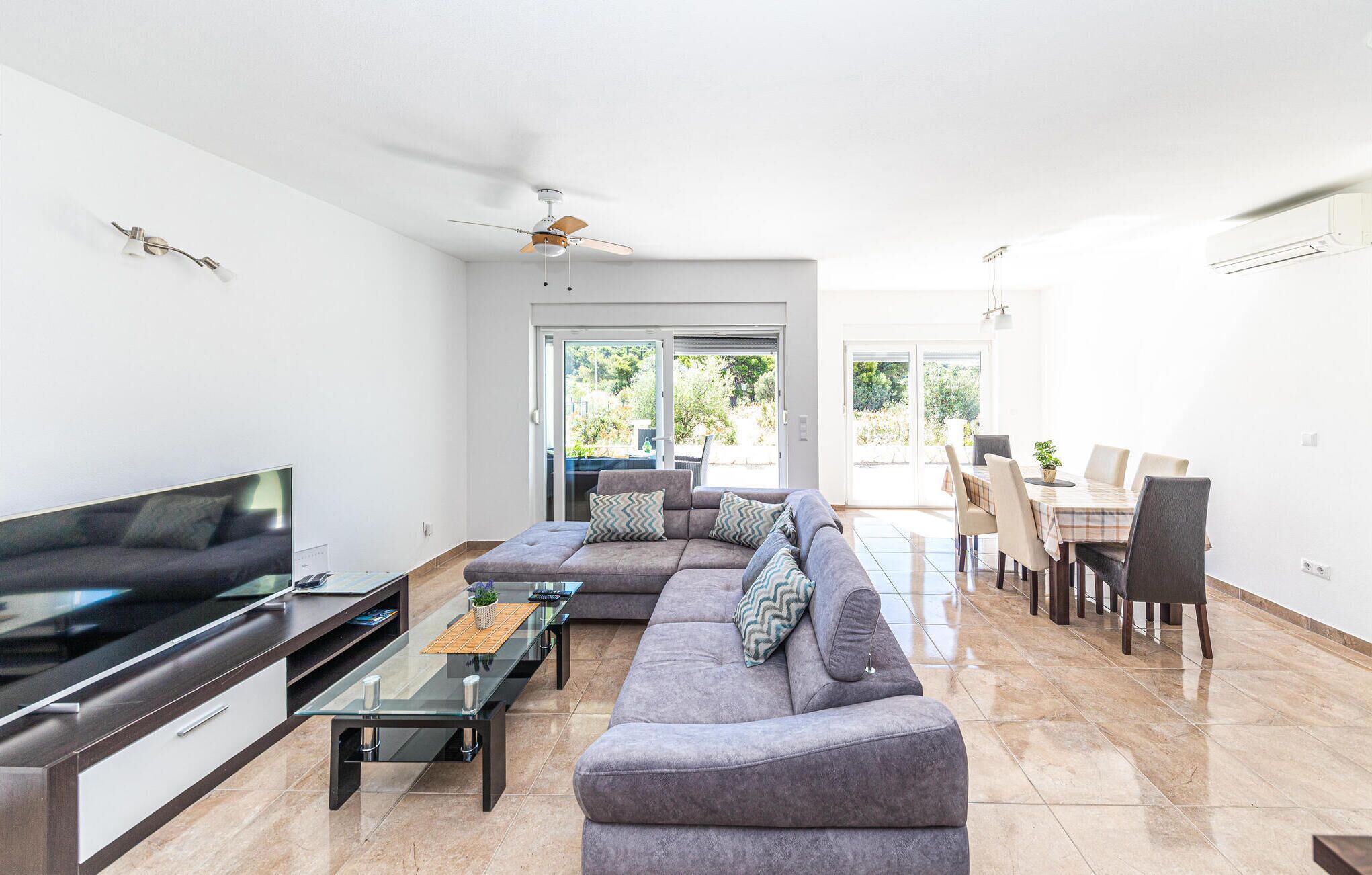 Een moderne woonkamer met een hoekbank, een glazen salontafel, een flatscreen televisie en een eethoek met een tafel en stoelen.