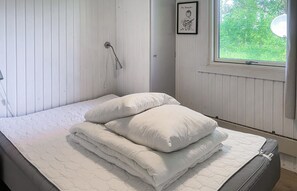 Cozy retreat with a single bed, wall-mounted showerhead, and a window offering a view of lush greenery.