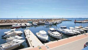 A marina with various boats docked, a rocky breakwater, and a clear blue sky.