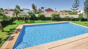 A rectangular swimming pool with clear blue water, surrounded by a tiled deck and a well-maintained lawn with palm trees.