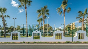 A row of white structures with windows, surrounded by palm trees and a clear blue sky.