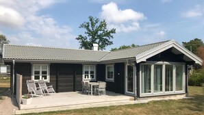 A modern house with a covered patio, a dining area, and a large windowed room.