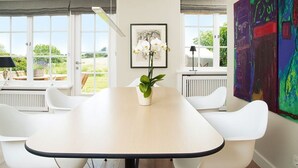 A modern dining area with a large table, white chairs, a potted plant, and artwork on the walls. - Hiidbloom-Hüs from A&M - Hiidbloom-Hüs (Kampen (Sylt))