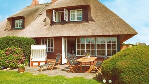 A thatched-roof house with a patio, outdoor seating, and a large window. - Hiidbloom-Hüs from A&M - Hiidbloom-Hüs (Kampen (Sylt))