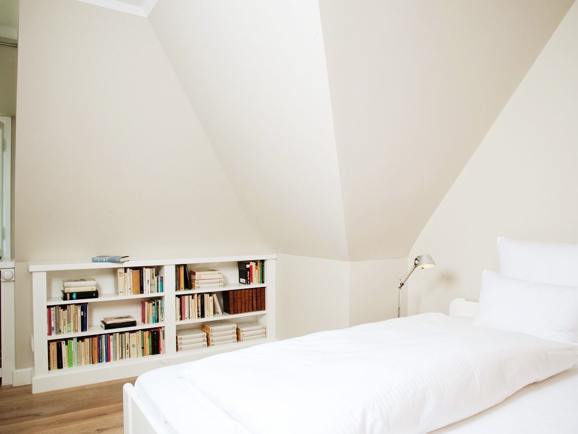 A bedroom with a white bed, a bookshelf, and a desk lamp.