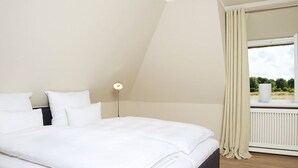 A bedroom with a large bed, a nightstand, a lamp, and a window with curtains. - Hiidbloom-Hüs from A&M - Hiidbloom-Hüs (Kampen (Sylt))