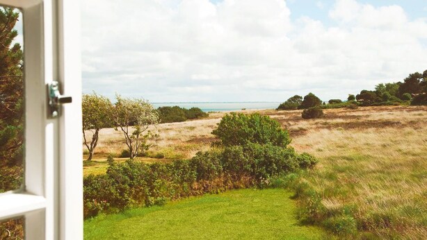 A view from a window overlooking a grassy field with trees and a distant body of water. - Hiidbloom-Hüs from A&M - Hiidbloom-Hüs (Kampen (Sylt))