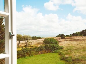 A view from a window overlooking a grassy field with trees and a distant body of water. - Hiidbloom-Hüs from A&M - Hiidbloom-Hüs (Kampen (Sylt))