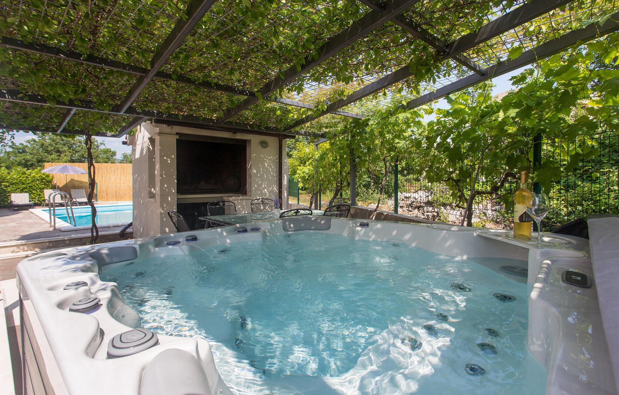 A hot tub with a pergola overhead, a pool, and outdoor furniture.