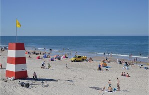 A beach with a lifeguard tower, a yellow vehicle, and people enjoying the sand and water. - Nice home in Ringkøbing with kitchen (Ringkøbing)