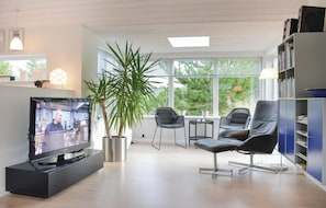 A modern living room with a flat-screen TV, a large potted plant, two black chairs, a small table, and a bookshelf. - Nice home in Ringkøbing with kitchen (Ringkøbing)