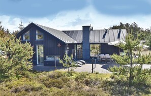 Una casa moderna con una terraza grande, una chimenea y un comedor con mobiliario exterior.