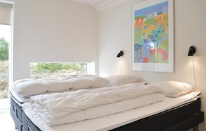 Un dormitorio con cama, dos lámparas de noche, una ventana y un cuadro abstracto y colorido en la pared.