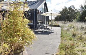 A wooden cabin with a patio, two lounge chairs, and a white umbrella. - Nice home in Ringkøbing with kitchen (Ringkøbing)