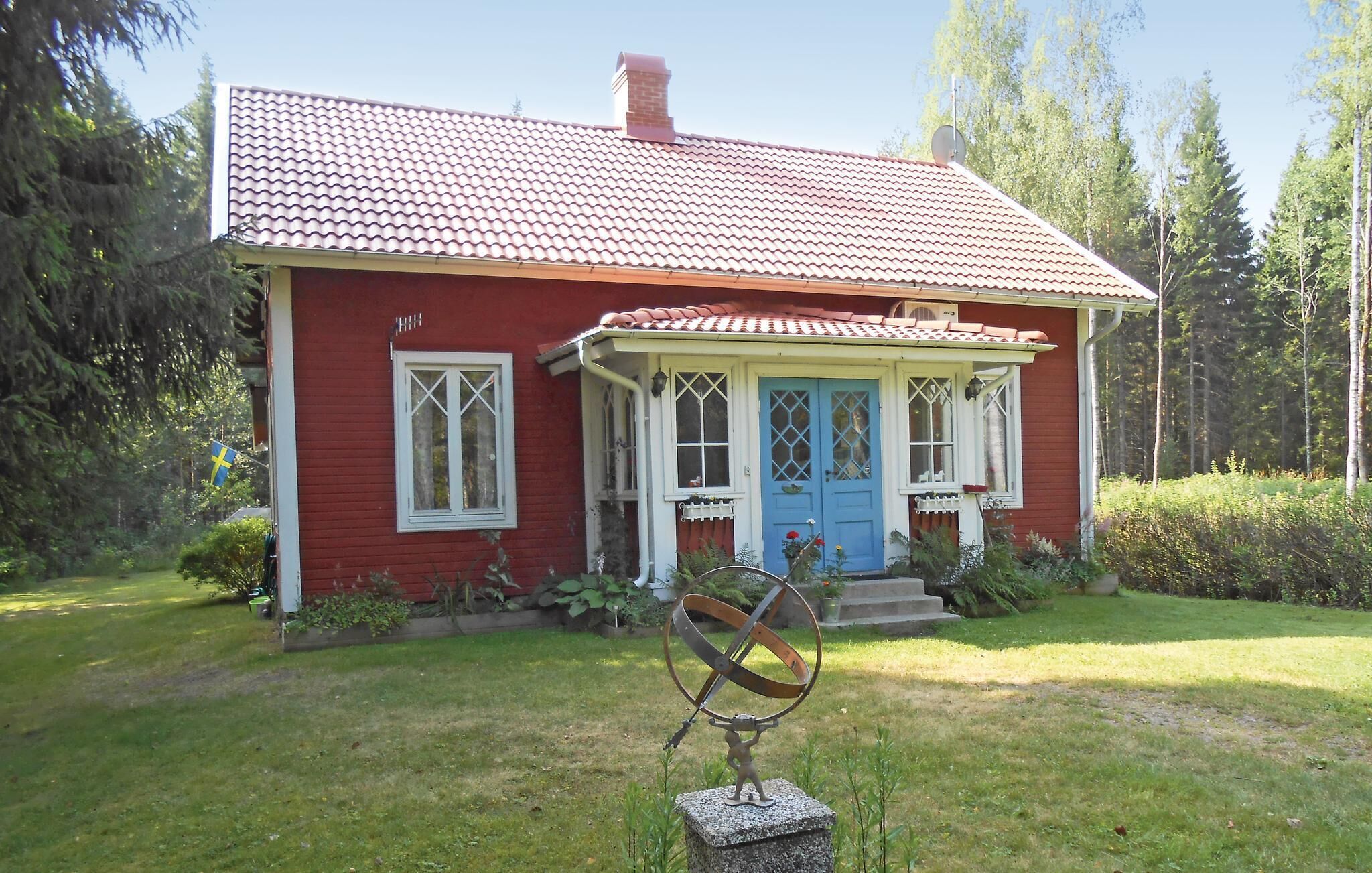 Una casa roja con puerta azul y ventanas blancas, rodeada de un jardín y árboles.