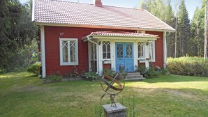 A red house with a blue door and white windows, surrounded by a garden and trees.