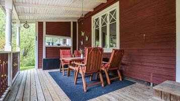 A covered porch with wooden furniture and a window with shutters.